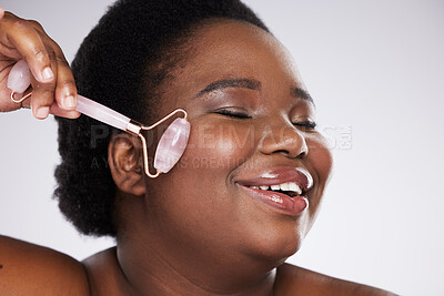 Buy stock photo Black woman, studio and skincare, rose quartz roller for cosmetic beauty, smooth and healthy glow on face. Model, happy and massage skin for health, wellness and beauty by gray background with smile