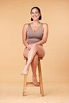 Portrait, beauty and an asian woman on a chair in studio on a beige background for natural body positivity. Model, underwear and an attractive young female sitting on a stool with confidence