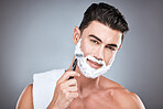 Face, razor and man with shaving cream in studio isolated on a gray background. Beard care, towel and portrait of male model with facial product, foam or gel to shave for wellness and hair removal