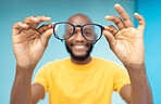 Hands, glasses and vision with a black man in studio on a blue background for prescription frame lenses. Spectacles, eyesight and eyewear with a male indoor to promote new round frames for seeing