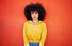 Portrait of woman with natural hairstyle on red background, headshot of model and red copy space. Confident young person with serious expression, curly hair and aesthetic fashion on studio wall