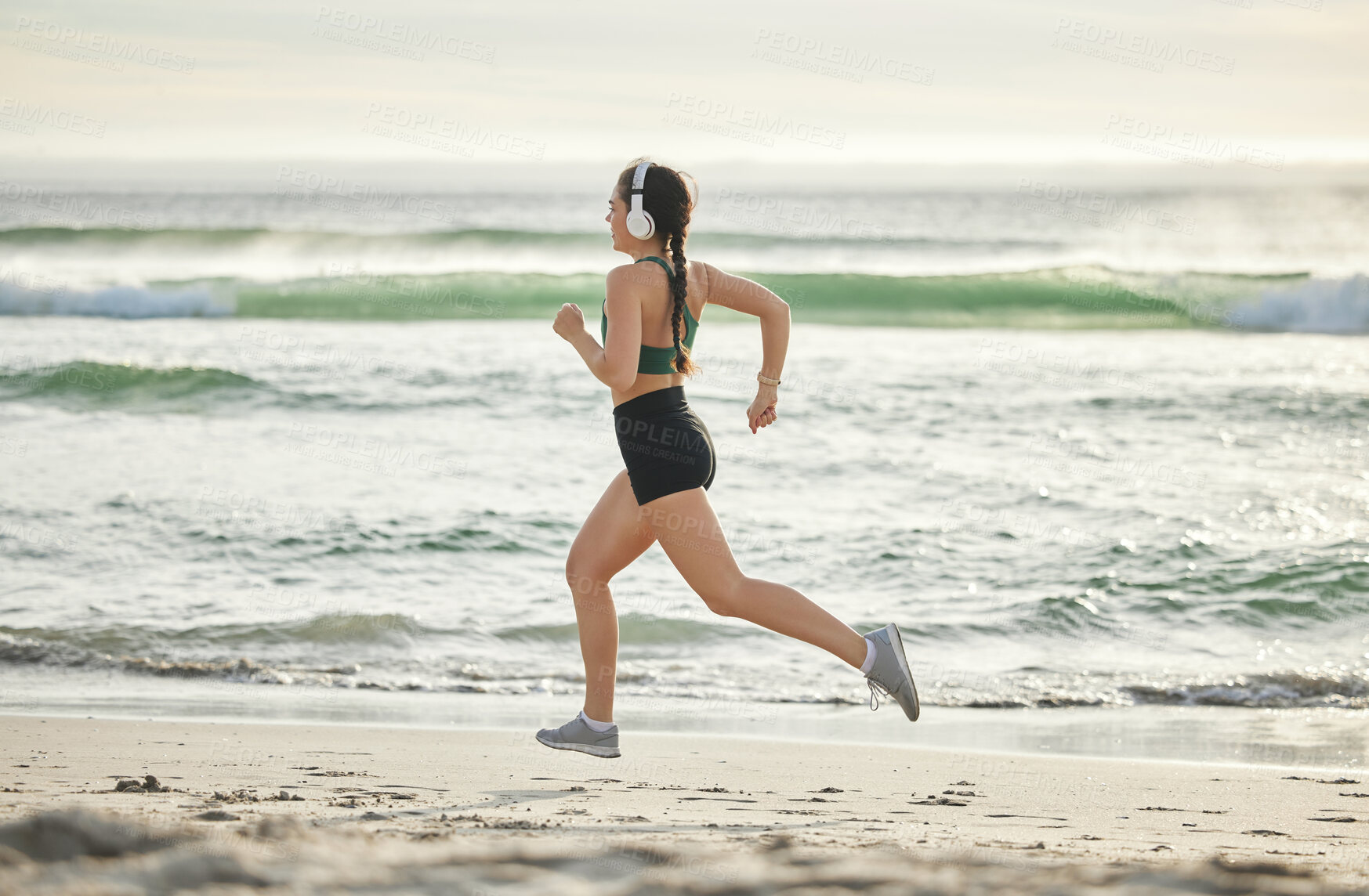 Buy stock photo Woman running on beach, listening to music and morning cardio routine for healthy lifestyle in California. Fitness workout by sea, young athlete with headphones and sports exercise in summer