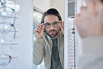 Optometry, glasses choice and man check mirror for vision, eye care and customer experience in store with lens frame. Young client or person eyes healthcare, retail and shop test for optical wellness