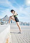 Fitness, woman and stretching legs in Cape Town for running, exercise or cardio workout by the beach. Active female runner in warm up leg stretch preparation for run, exercising or training in nature