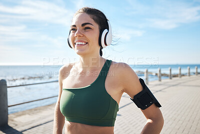 Buy stock photo Happy, fitness and woman with music at beach for running, exercise and cardio on blue sky background. Radio, podcast and workout run by girl at ocean for training, smile or relax in audio motivation