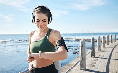 Buy stock photo Headphones, smartwatch and woman running for workout, exercise and health results, progress or fitness steps. Goals, check timer and sports person at beach listening to music or podcast for training