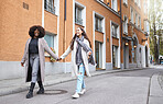 Woman, friends and holding hands in the city for travel, friendship or fun journey in the street. Happy women walking, touching hand and smiling in happiness for traveling together in a urban town