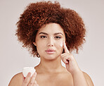 Skincare, beauty and portrait of woman with lotion on face, and afro, advertising luxury skin product promotion. Dermatology, cosmetics and facial for model holding jar isolated on studio background.