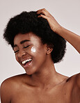 Skincare, cream on face and black woman with hand on hair, smile and afro, advertising luxury skin product promotion. Dermatology, cosmetics and facial for happy model isolated on studio background.