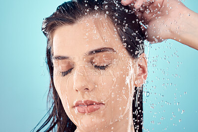 Buy stock photo Water splash, hair care and face of woman in shower in studio isolated on a blue background. Beauty, eyes closed and young female model washing, cleaning or bathing for hygiene, skincare and health.