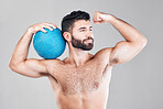 Sport, fitness and man with ball flexing arm, topless and isolated on grey background. Exercise, motivation and sports coach or personal trainer with workout mindset for training in studio with smile