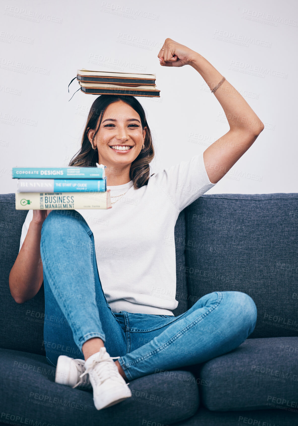 Buy stock photo Portrait, education and success with a student woman flexing her bicep while sitting on a sofa in her home. University, books and balance with an attractive young female pupil feeling confident