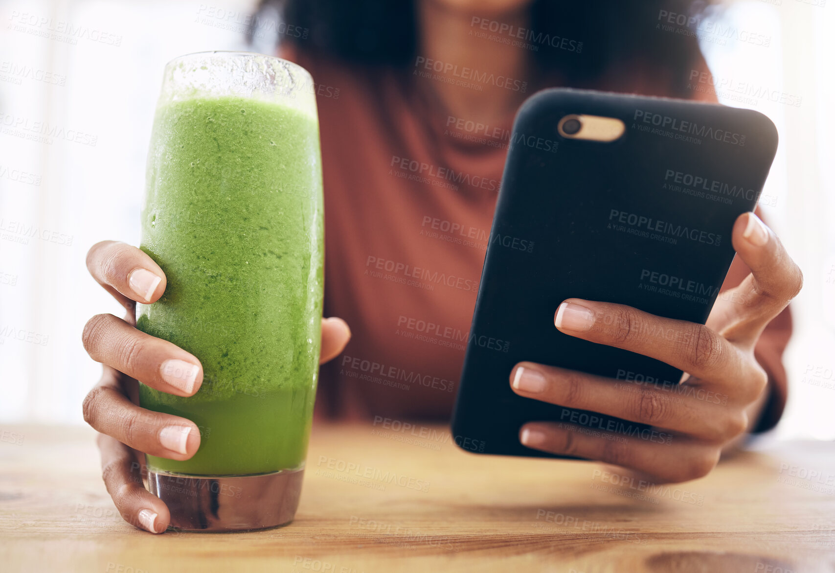 Buy stock photo Hands, smoothie and phone with a black woman in the kitchen of her home for health, weight loss or nutrition. Mobile, glass and wellness with a female posting a status update on social media