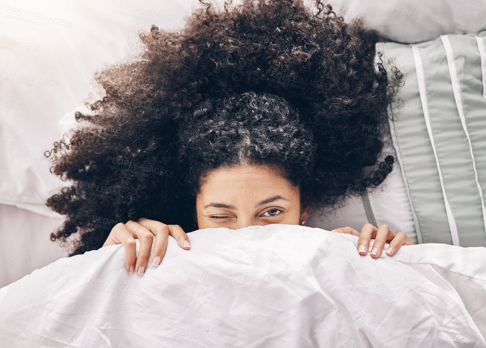 Buy stock photo Bed, wink portrait and black woman in the morning after sleep and  rest at home with blanket. Eyes, house and wake up happiness of a young person hiding face under the bedroom covers on a pillow