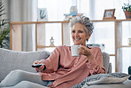 Senior woman, sofa and coffee to relax with remote for television, video or movies with smile in house. Elderly lady, couch and tea with happiness in home living room for watching tv in retirement