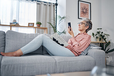 Buy stock photo Elderly woman check phone, communication and relax at home, social media with technology and reading book. 
Retirement, internet and chat online with wifi, text message or email with news website
