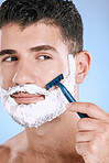 Shaving, beard and cosmetic man with cream for grooming isolated on a blue background. Skincare, beauty and model with razor to shave hair on face with foam for a clean facial look on a backdrop