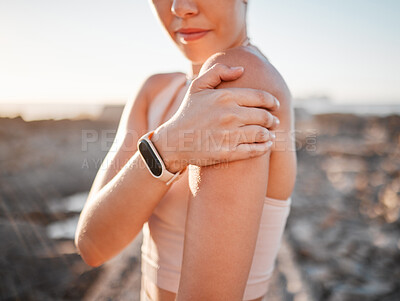 Buy stock photo Beach, fitness and woman with hand on shoulder pain standing on rocks at ocean. Nature, sports and injury during workout for health and wellness, muscle trauma during stretching exercise in morning.