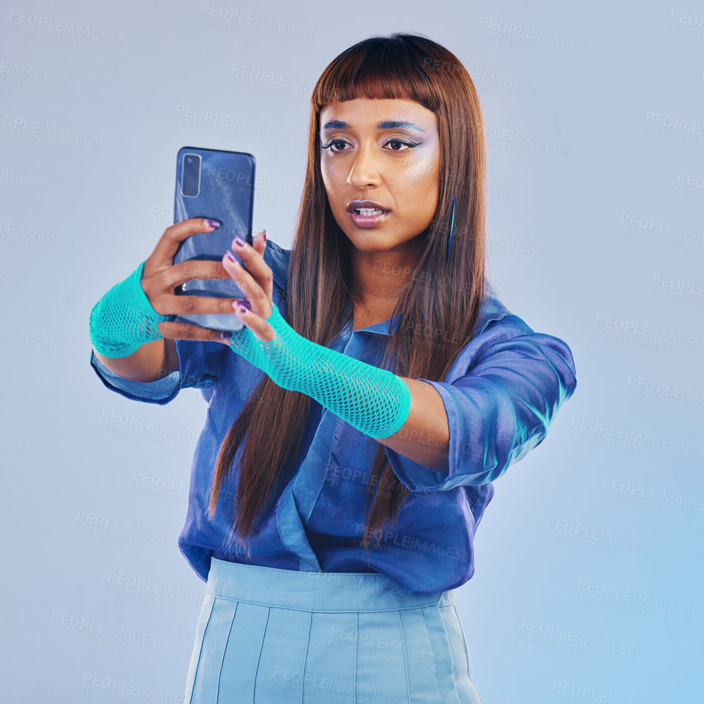 Buy stock photo Fashion, selfie and woman with smartphone and cyberpunk neon clothing isolated on blue background. Social media, future and trendy gen z influencer from India with phone in studio for profile picture