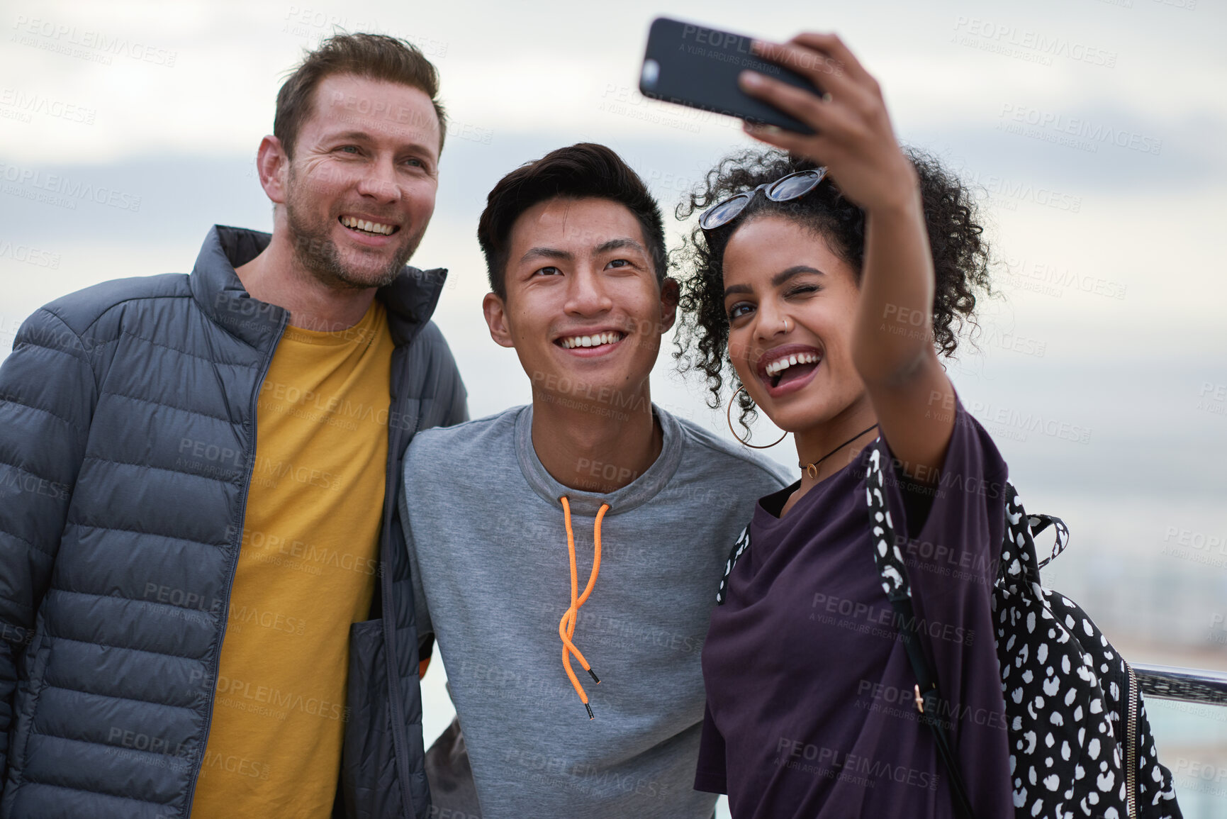 Buy stock photo Men, black woman and friends selfie at beach for holiday travel, together and smile for internet blog post. Outdoor adventure, phone and profile picture for social media app by ocean with diversity