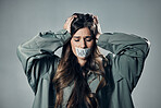 Woman, protest and tape on mouth in fear for cold war, armageddon or doomsday against gray studio background. Female activist with hands on head and message to stop or end global violence in society