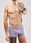 Fitness, muscle and man body in studio with fitness, exercise and workout aesthetic. Isolated, gray background and studio with a sexy, strong and young male model in underwear with tattoos and abs