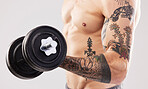 Arm muscle, dumbbell and man with tattoo and workout in a studio for fitness, exercise and power. Gray background, isolated and gym model weightlifting, bodybuilding and doing body wellness training