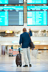 Black man, airport and pointing at flight schedule display, waiting in terminal for international business trip. Check in, travel and businessman checking international destination departure time.