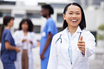 Thumbs up, happy and portrait of a doctor outdoor of the hospital with a leadership mindset. Happy, smile and Asian female healthcare worker with a success or agreement gesture in a medical clinic.