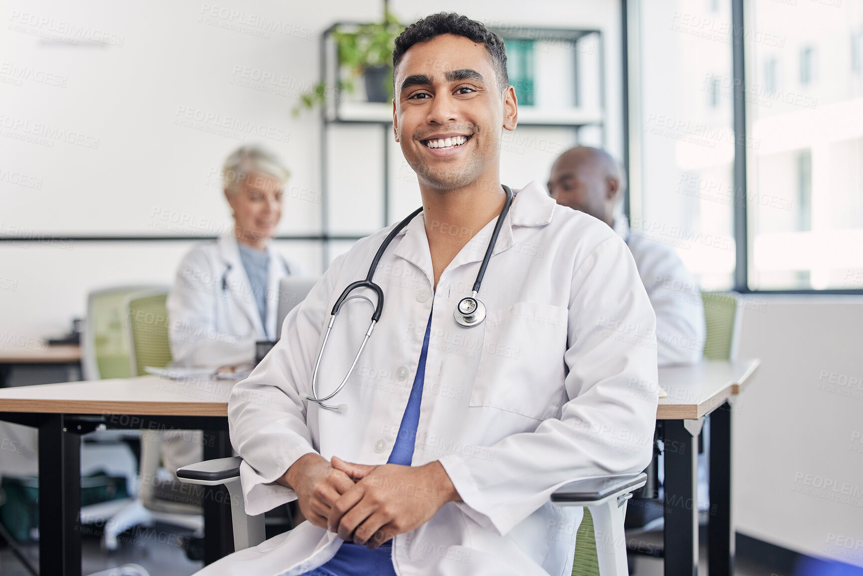 Buy stock photo Young doctor, man and portrait at hospital desk with smile for healthcare, planning and teamwork. Professional leader, doctors and expert in health, wellness and happy in clinic with group at table