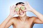 Beauty, skincare and kiwi on eyes of woman feeling silly from fruit, wellness and vitamin c health. isolated, blue background and smile in studio of a young model happy about green cosmetic treatment
