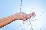 Hands, water splash and wash for skincare hygiene or hydration against a blue studio background. Closeup of hand with liquid drops, shower or washing for clean wellness, natural health and self care