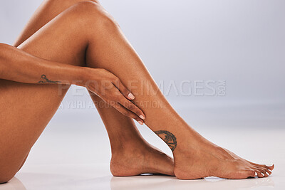 Buy stock photo Hand, legs and body with a black woman in studio, sitting on the floor against a gray background for skincare. Fitness, beauty and tattoo with a female posing alone for hair removal, laser or wax
