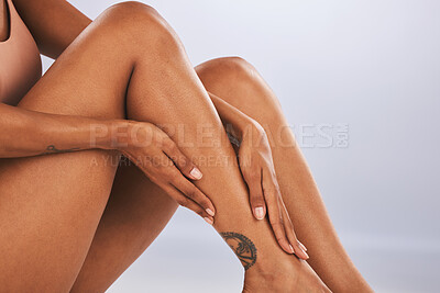 Buy stock photo Hands, legs and beauty with a black woman in studio, sitting on the floor against a gray background for skincare. Fitness, body and tattoo with a female posing for hair removal, wax or laser
