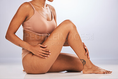 Buy stock photo Hands, legs and skincare with a black woman in studio, sitting on the floor against a gray background for beauty. Fitness, body and tattoo with a female posing for hair removel, wax or laser