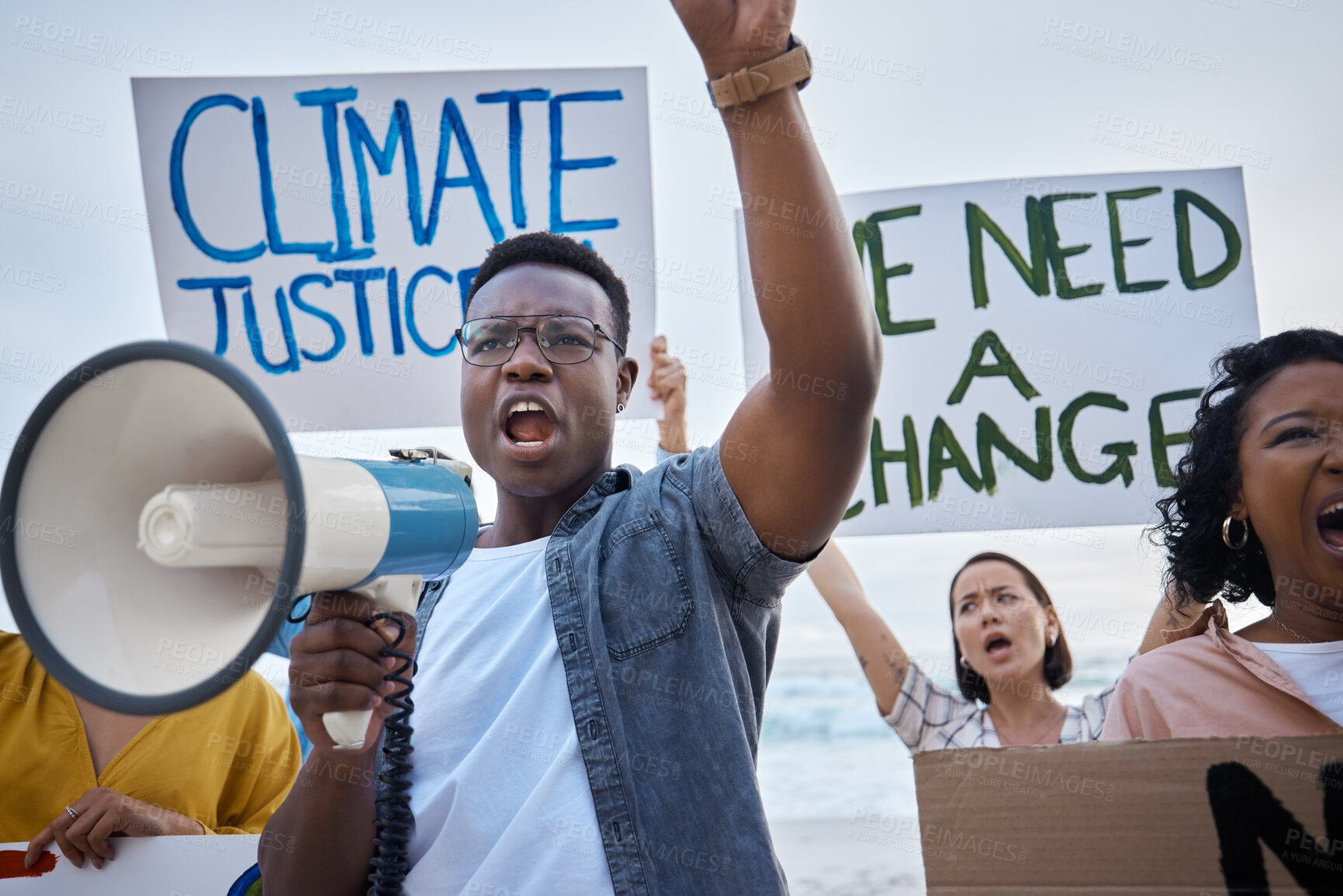 Buy stock photo Climate change poster, protest and black man with megaphone for freedom movement. Angry, crowd screaming and young people by the sea with world support for global, social and equality action at beach