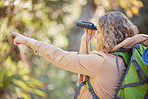 Woman hiking, forest and binoculars with point, vision and birdwatching on outdoor adventure in summer. Happy hiker girl, free and search in woods, forrest and focus on walk with backpack on holiday