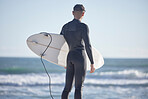Back, surfing man and standing at beach with board, freedom and summer waves with blue sky. Surfer guy at sea, sunshine and travel for water sports, adventure and ocean in nature 