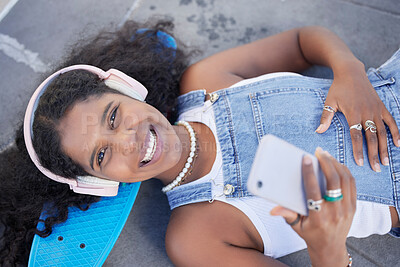 Buy stock photo Portrait, phone and music with a black woman skater lying on her board at a skatepark from above. Face, skating and social media with a female skateboarder resting on the ground during a break