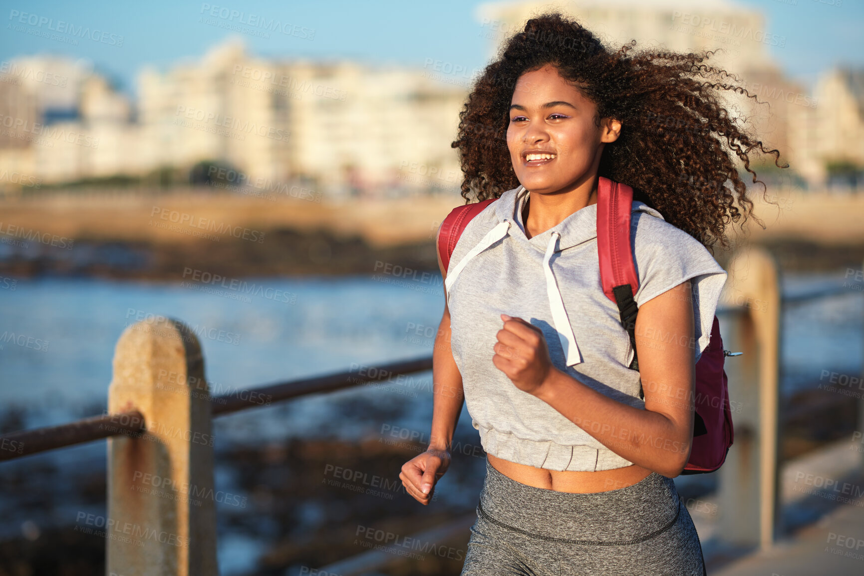 Buy stock photo Black woman runner, backpack and sea with smile and summer adventure in city. Gen z and student african girl, happy and young on travel, running and freedom by ocean promenade for fitness