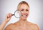 Portrait, beauty and magnifying glass with a woman in studio on a gray background to examine her skin. Face, zoom and smile with an attractive female cofident in her natural skincare treatment