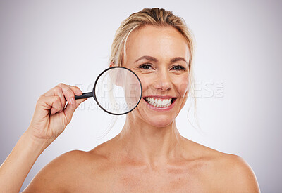 Buy stock photo Portrait, beauty and magnifying glass with a mature woman in studio on a gray background to examine her skin. Face, wrinkle and antiaging with an attractive female confident in her natural skincare