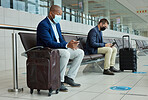 Social distance, suitcase and businessmen waiting in the airport and networking with cellphone. Face mask, luggage and professional male employees sitting with travel restrictions browsing on a phone