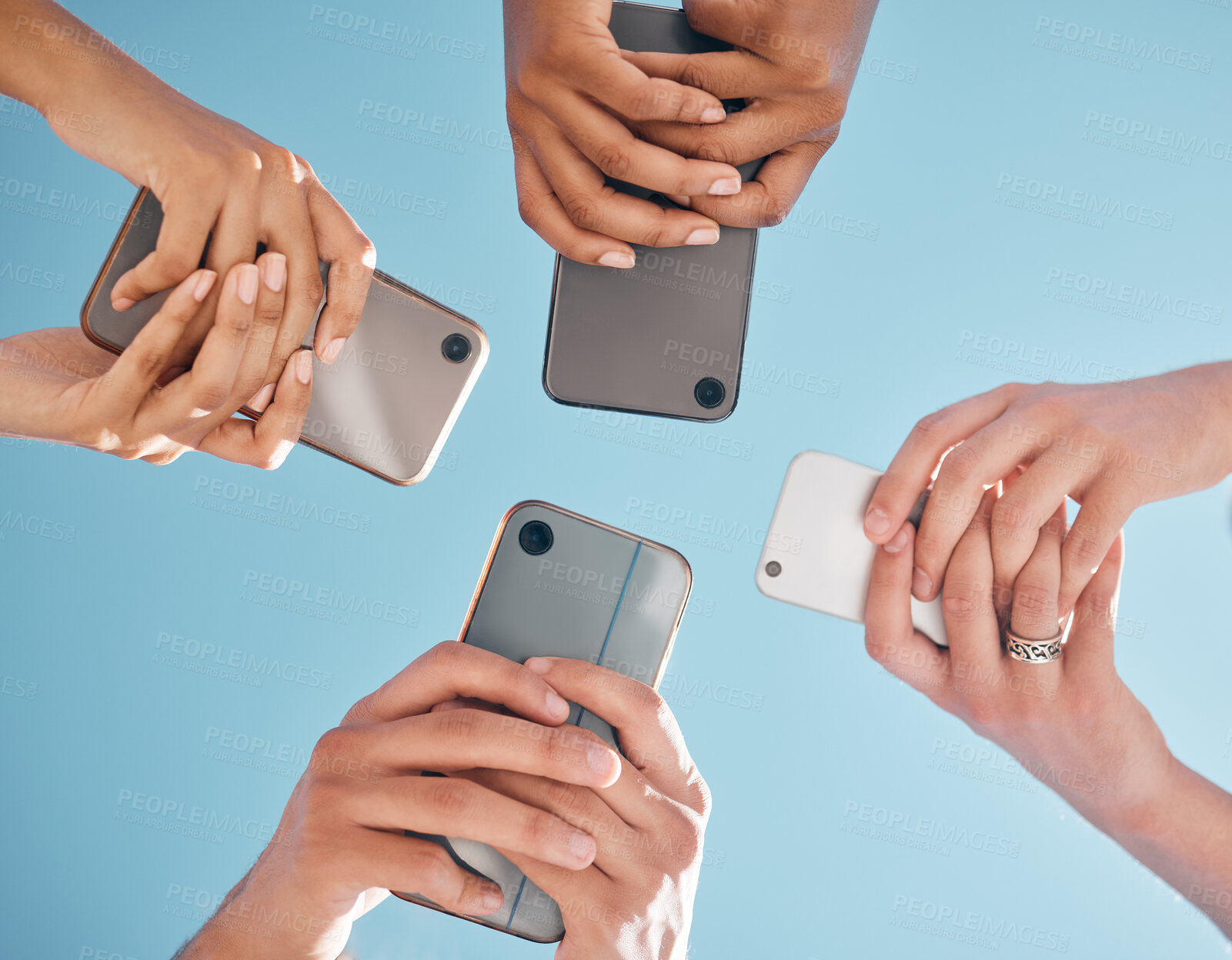 Buy stock photo Hands, phone and people networking below on social media or mobile app with blue sky background. Low angle hand of group with smartphone in circle for online share, data sync or team communication