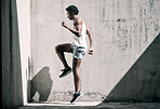 Exercise, fitness and black man jump in city for health, wellness and energy against wall mockup. Sports, training and male athlete jumping, workout or exercising for endurance, practice or strength.