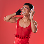 Dance, music and gay man with headphones isolated on a red background in a studio. Freedom, streaming and dancing lgbt person listening to a podcast, radio and audio on a backdrop for entertainment