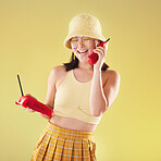 Landline, fashion and woman on a call in a studio with art eyes stickers on her face with 90s aesthetic. Communication, beauty and happy Asian female with a telephone isolated by a yellow background.