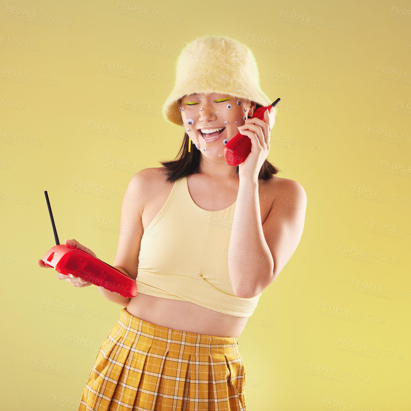 Buy stock photo Landline, fashion and woman on a call in a studio with art eyes stickers on her face with 90s aesthetic. Communication, beauty and happy Asian female with a telephone isolated by a yellow background.
