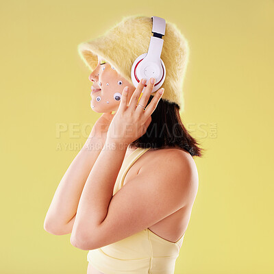 Buy stock photo Makeup, music headphones and woman in studio isolated on a yellow background. Eye stickers, freedom technology and young female model listening, enjoying and streaming radio, podcast and audio song.