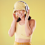 Music headphones, makeup and woman in studio isolated on a yellow background. Eye stickers, freedom technology and happy female model listening, enjoying and streaming radio, podcast and audio song.